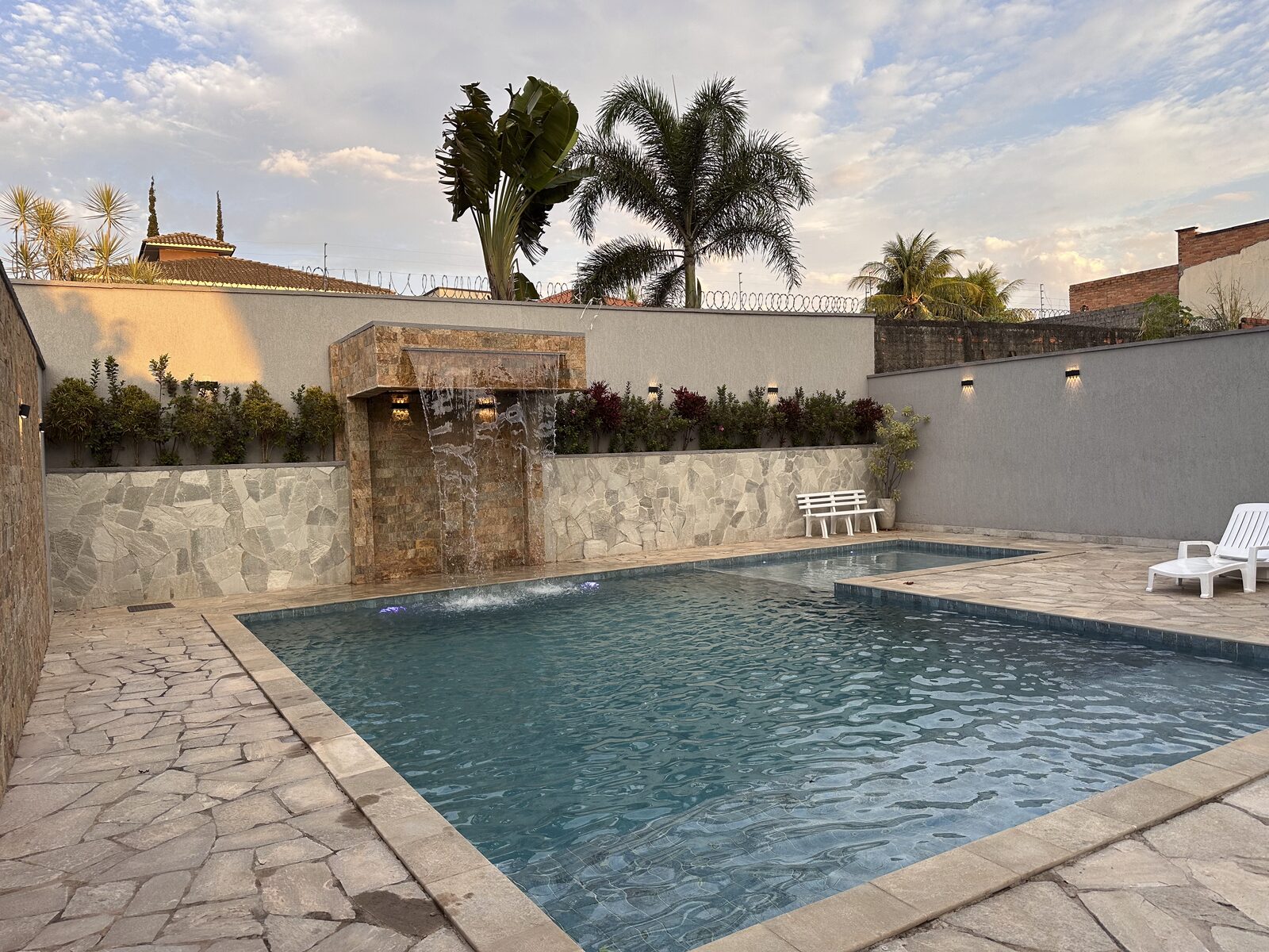 Piscina com cascata de pedra e ducha na área externa da Dream House Eventos, em Goiânia